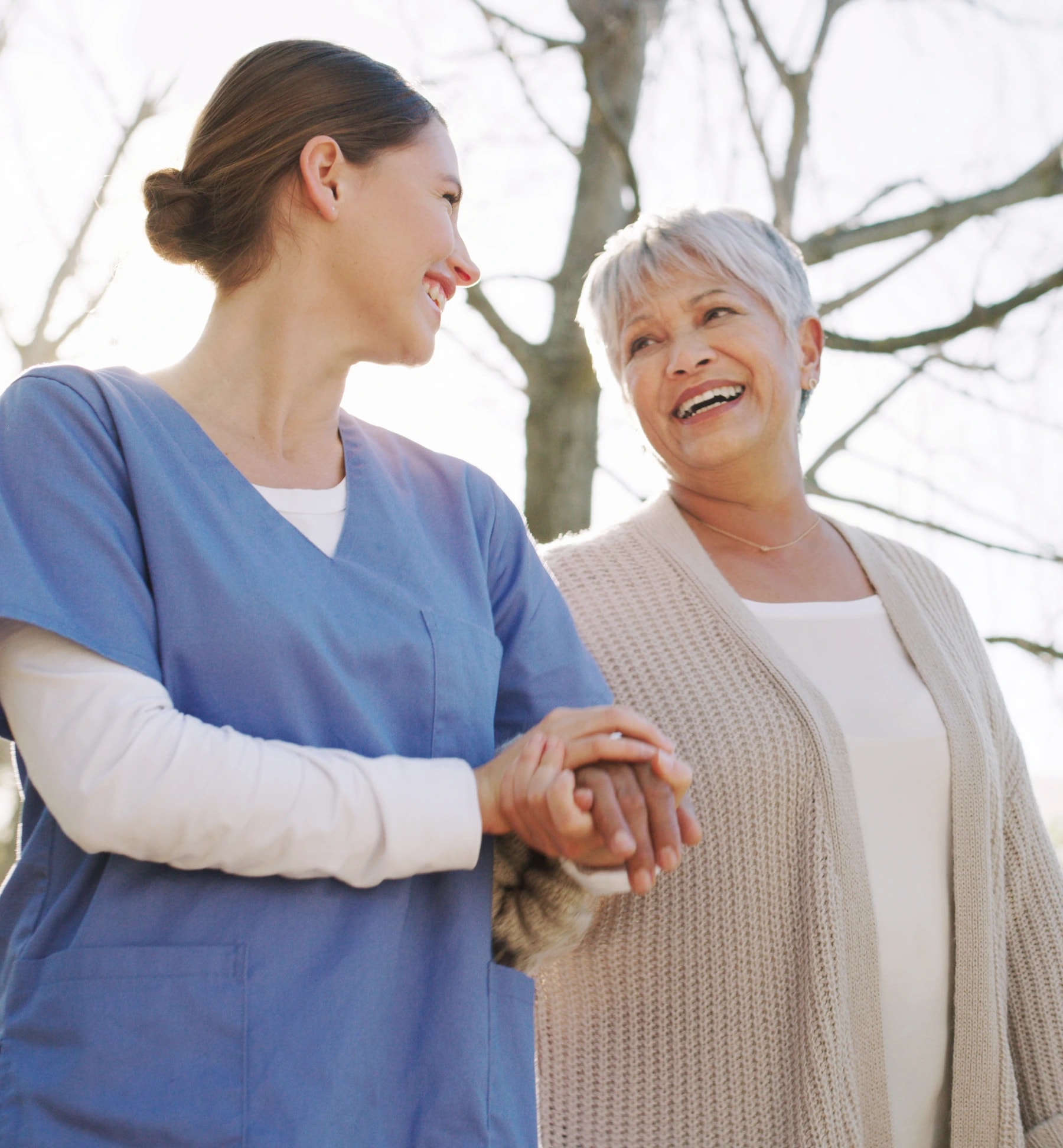 A caregiver in a blue uniform walking outdoors with an older woman.